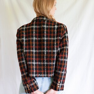 May include: A black, white, and orange plaid blazer with gold buttons. The blazer is cropped and has a slightly oversized fit.