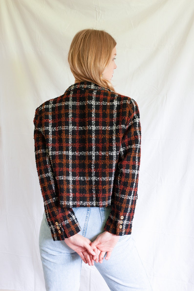 May include: A black, white, and orange plaid blazer with gold buttons. The blazer is cropped and has a slightly oversized fit.