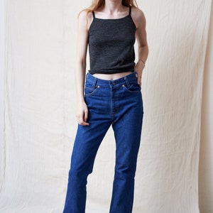 May include: A woman wearing a dark gray tank top and blue denim jeans with a flared leg.