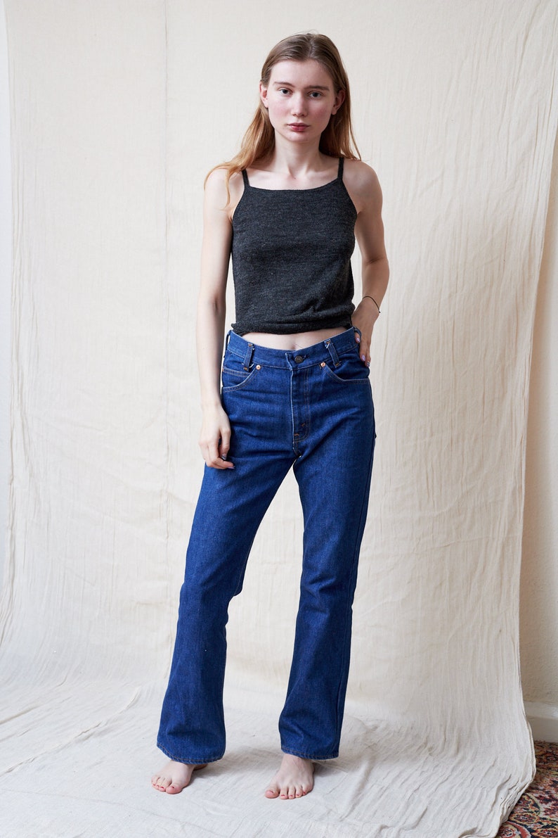 May include: A woman wearing a dark gray tank top and blue denim jeans with a flared leg.