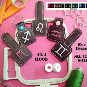 May include: A set of 12 zodiac sign key fob embroidery designs, each in a 4x4 inch hoop. The designs are shown on brown leather key fobs with white and pink stitching. The text "DIGITIZED BY HAND DESIGNS" is at the top of the image. The text "KEY FOB DESIGN SET ALL 12 SIGNS INCLUDED" is at the bottom of the image.