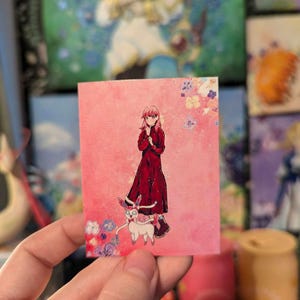 Può includere: Una carta rosa e bianca con un'illustrazione di cartone animato di una ragazza con un vestito rosso e un animale bianco con le orecchie rosa. La ragazza tiene le mani giunte davanti a sé e l'animale la sta guardando. Lo sfondo è un acquerello rosa con fiori bianchi.