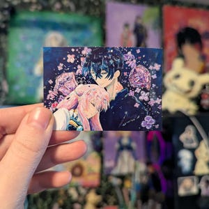 Könnte beinhalten: Ein rechteckiger Kunstdruck im Anime-Stil mit einem sich umarmenden Paar, umgeben von rosa und lila Blumen auf einem dunkelblauen Hintergrund. Das Kunstwerk hat einen weichen, malerischen Stil mit detaillierten Charakterdesigns.