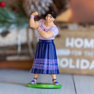 May include: A figurine of a person with purple and blue clothing, flexing their bicep. The person is wearing a purple shirt with a red design, a blue skirt with a purple and red pattern, and purple shoes. The figurine is standing on a green base.