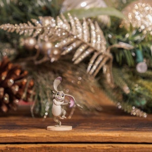 May include: A small gray rabbit figurine with large ears and a friendly expression. The figurine is standing on a round base and is posed with its right leg raised.