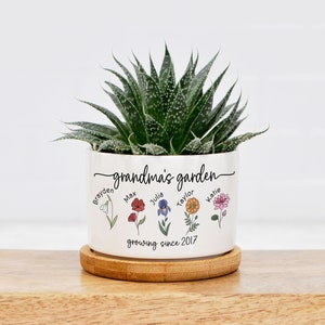 May include: White ceramic planter with the text "grandma's garden" and five flowers with names written below each flower. The names are:  Broyden, Max, Julia, Taylor, and Katie. The text "growing since 2017" is written below the flowers.