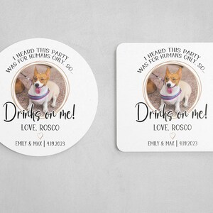 May include: Round white coaster with a photo of a dog in a red and white striped shirt. The text reads "I heard this party was for humans only. So... Drinks on me! Love, Roscoe. Emily & Max | 4.19.2023"