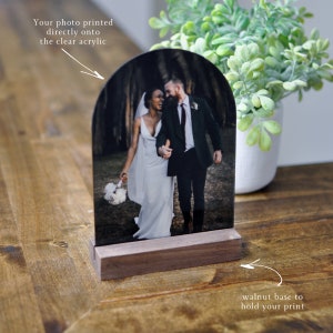 Puede incluir: Una foto de boda impresa directamente en un arco de acr&iacute;lico transparente, montada sobre una base de nogal. La foto muestra a una pareja caminando por un bosque.