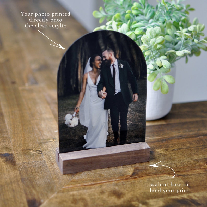 Puede incluir: Una foto de boda impresa directamente en un arco de acr&iacute;lico transparente, montada sobre una base de nogal. La foto muestra a una pareja caminando por un bosque.