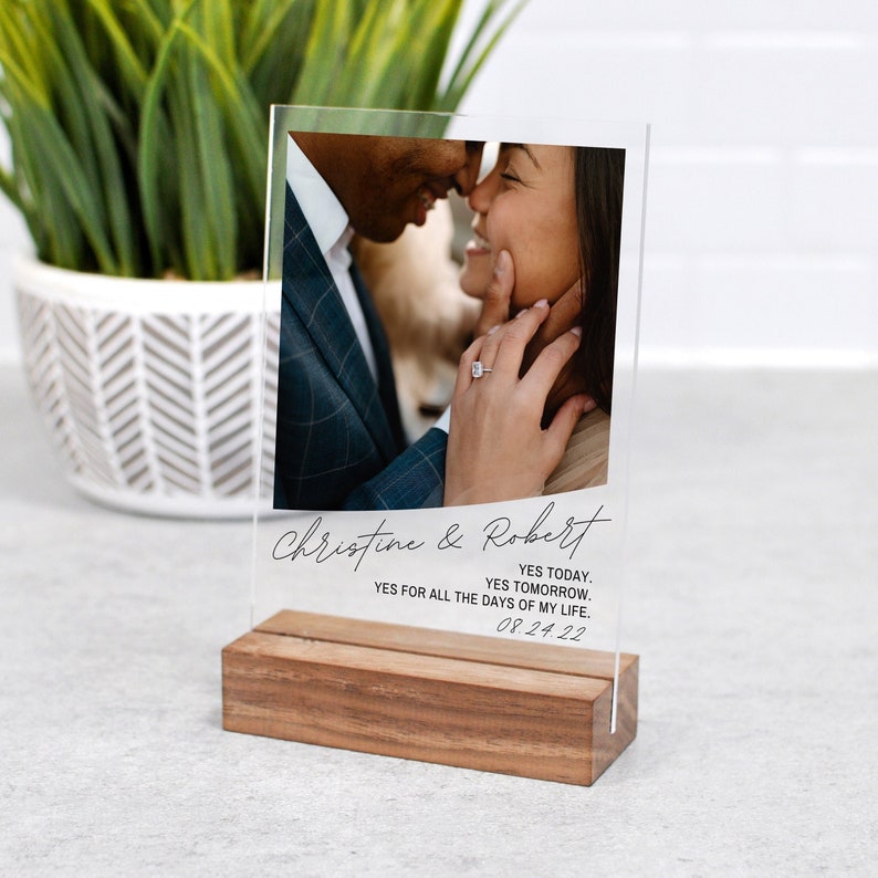 May include: A clear acrylic photo display with a wooden base. The photo shows a couple embracing, with the names "Christine & Robert" and the date "08.24.22" printed below. The text reads "YES TODAY. YES TOMORROW. YES FOR ALL THE DAYS OF MY LIFE."