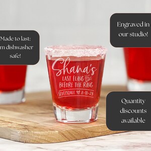 Puede incluir: Vasos de chupito llenos de l&iacute;quido rojo, con borde blanco y grabados con texto. El vaso central dice "Shana's LAST FLING BEFORE THE RING Scottsdale 8-11-23". Los vasos est&aacute;n sobre una tabla de madera.
