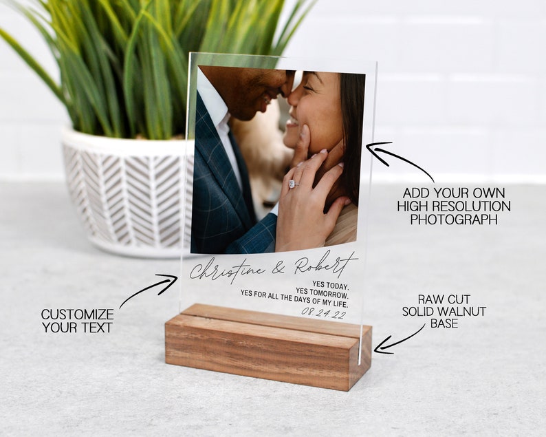 May include: A clear acrylic photo display with a raw-cut solid walnut base. The display features a photograph of a couple and includes the text "Christine & Robert" and the date "08.24.22". The text "Customize Your Text" is also visible.