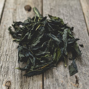Può includere: Un mucchio di foglie di tè verde essiccate su una superficie di legno invecchiato.