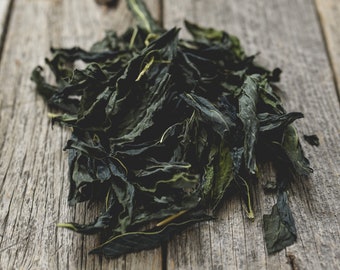 May include: A pile of dried green tea leaves on a weathered wooden surface.
