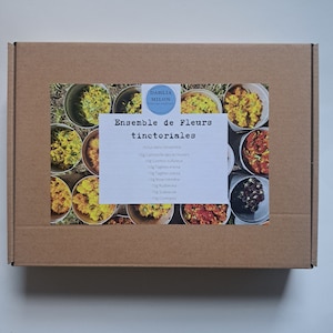 Peut inclure: Une boîte en carton avec une étiquette indiquant "Ensemble de Fleurs tinctoriales" et listant les ingrédients inclus dans l'ensemble : 10 g de camomille des teinturiers, 10 g de cosmos sulfureux, 10 g de tagètes dressées, 10 g de tagètes patules, 10 g de rose trémière, 10 g de rudbeckia, 10 g de scabieuse, 10 g de coreopsis. La boîte est remplie de fleurs séchées.