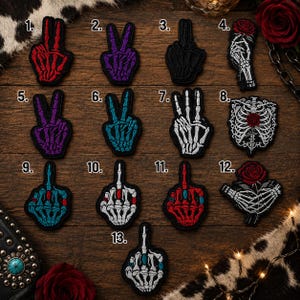 May include: Thirteen embroidered patches featuring skeleton hand designs. Styles include peace signs, middle fingers, and skeleton hands holding red roses, or a rib cage with a rose. Colors include red, purple, black, white, and teal on dark backgrounds.
