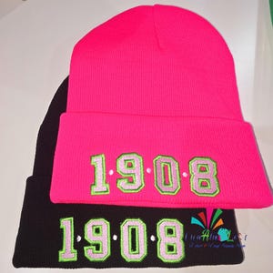 May include: Two black and pink knit beanies with the number "1908" embroidered in green and white on each.