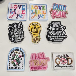 May include: A collection of eight embroidered patches featuring religious text and floral designs. The patches include phrases like Love Like Jesus, Faith Over Fear, Be Light, and various Bible verses in colorful, black, and white thread styles.