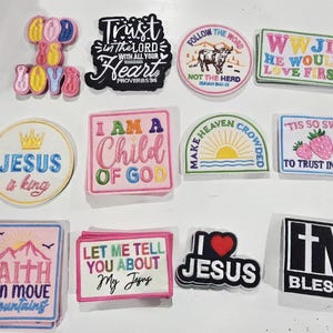 May include: A collection of twelve embroidered patches featuring religious themes and text. Designs include phrases like 'God is Good', 'Trust in the Lord', 'Jesus is King', 'I am a Child of God', 'Faith Can Move Mountains', 'I Love Jesus', and 'I'm Blessed'.