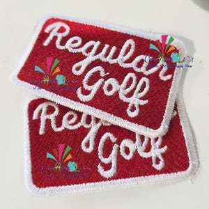 May include: Two rectangular red embroidered patches with white cursive text that reads "Regular Golf". The patches have a white border and are stacked on top of each other.