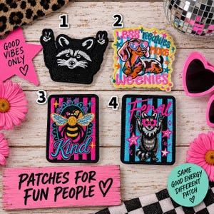 May include: Four embroidered patches featuring various designs: a black raccoon with peace signs, a dachshund wearing heart-shaped glasses with the text 'LESS MEANIES MORE WEENIES', a bee with the word 'Kind', and a raccoon with the word 'Feral'.