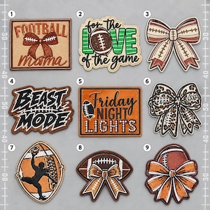 May include: A collection of nine embroidered patches featuring football-themed designs, including bows, text like 'Football Mama' and 'Beast Mode', and football graphics in brown, white, black, and green colours, arranged in a grid on a grey background.
