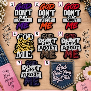 May include: A collection of eight iron-on patches featuring the text God Don't Play About Me in various colors and styles, including purple, orange, red, gold, and sequined designs, arranged on a wooden surface with decorative floral accents.