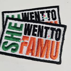May include: Two embroidered patches with the text "SHE WENT TO FAMU". The patches have a white background with black, green, and orange lettering and a black border. The patches are rectangular.