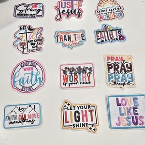 May include: A collection of eleven rectangular and shaped embroidered patches featuring various religious phrases and colorful designs. The patches include text such as She Is Strong, Just Jesus, Spirit Lead Me, Be Still, Stronger Than The Storm, Faith Is Essential, Worry Ends When Faith Begins, Worthy Is Your Name, Pray On It, Faith Can Move Mountains, Let Your Light Shine, and Love Like Jesus.