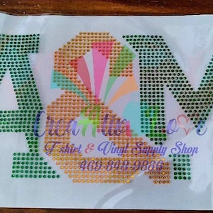May include: A green and gold rhinestone iron-on design featuring the letters "A&M".