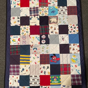 May include: A blue and white patchwork quilt with a variety of colorful squares. The squares feature different patterns, including plaid, stripes, and cartoon characters. The quilt is edged with a dark blue border.