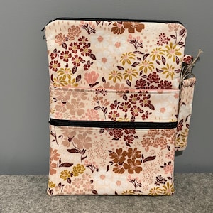 Puede incluir: Una bolsa con cremallera de tres compartimentos, con un estampado floral en tonos rosa, marrón y dorado. La bolsa tiene una cremallera negra y un pequeño bolsillo con cremallera adjunto.