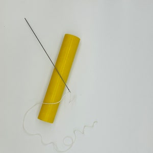 Op de afbeelding: Een gele cilinder met een witte draad en een zilveren naald die er doorheen gaat.