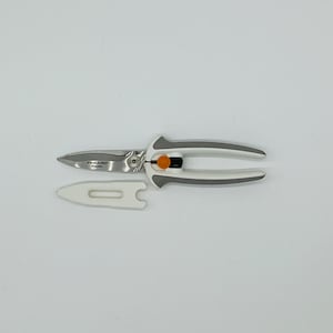 May include: White and grey kitchen shears with an orange handle. The shears have a safety lock and a blade guard.