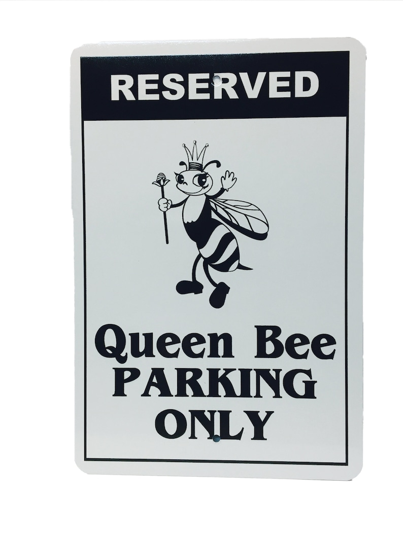 Puede incluir: Un letrero de metal blanco con texto negro y una abeja de dibujos animados con una corona. El letrero dice "RESERVED Queen Bee PARKING ONLY".