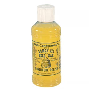 May include: A clear plastic bottle filled with yellow lemon oil furniture polish. The label reads Old Craftsmen's Brand Lemon Oil with Bees Wax, Restores Full Lustre to Fine Furniture, and Net Contents 8 oz., 240 ml with a beehive graphic.