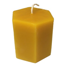 May include: A hexagonal beeswax candle with a white wick. The candle is a deep yellow colour.