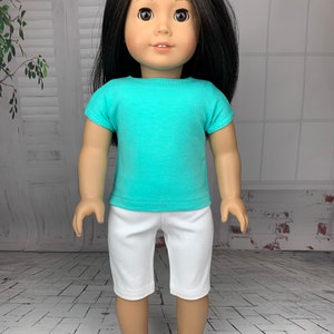 May include: A doll wearing a turquoise short-sleeved shirt and white shorts. The doll has long black hair and brown eyes.