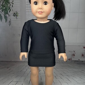 May include: A black long-sleeved dress for a doll. The dress has a round neckline and is made of a stretchy fabric.