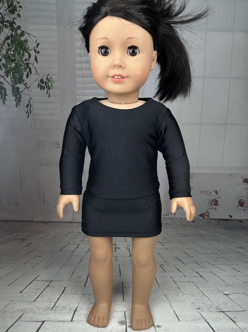 May include: A black long-sleeved dress for a doll. The dress has a round neckline and is made of a stretchy fabric.