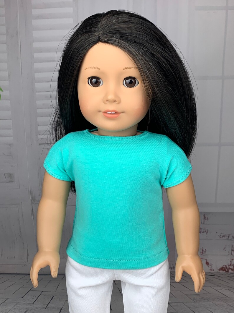 May include: A doll wearing a turquoise short-sleeved t-shirt and white pants.