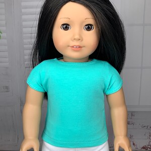 May include: A doll wearing a turquoise short-sleeved shirt and white pants.
