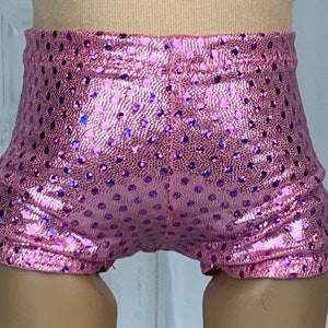 May include: Pink sparkly shorts with a polka dot pattern. The shorts are made of a shiny fabric and have a stretchy waistband.