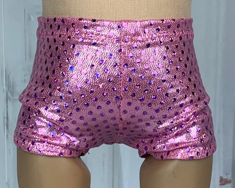 May include: Pink sparkly shorts with a polka dot pattern. The shorts are made of a shiny fabric and have a stretchy waistband.