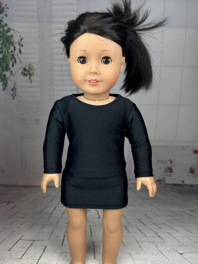 May include: A black long-sleeved dress with a round neckline, worn by a doll with black hair.
