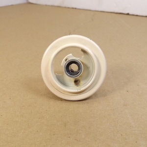 May include: Off-white plastic gear with a toothed outer edge and a central metal bearing. The gear has a circular design with a curved opening and is set against a neutral background.
