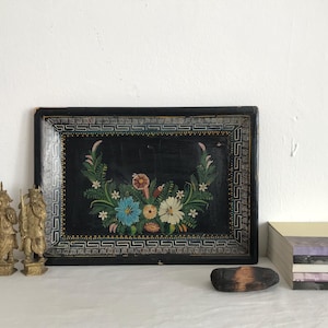 May include: A black wooden tray with a painted floral design in shades of pink, blue, green, and yellow. The tray has a black and gold border with a geometric pattern.