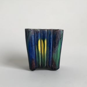 Puede incluir: Un pequeño macetero de cerámica azul, verde y amarillo con un diseño ondulado.