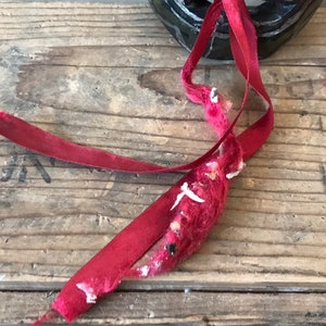 May include: Close-up of a red ribbon tied around a wooden box. The ribbon is frayed and worn, with some of the fibers coming loose.