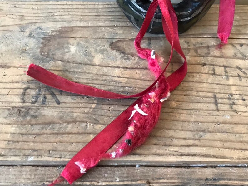 May include: Close-up of a red ribbon tied around a wooden box. The ribbon is frayed and worn, with some of the fibers coming loose.